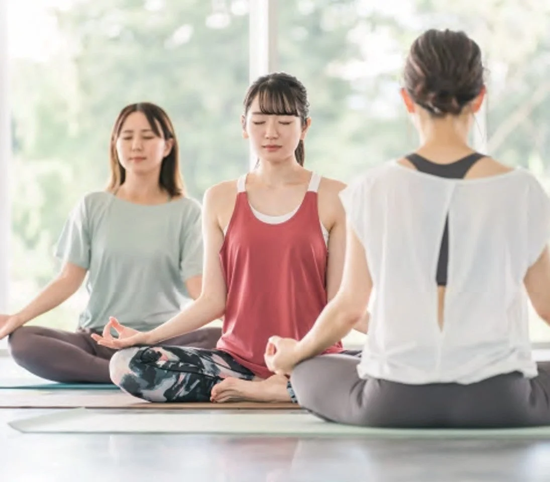 明るい室内で3人の女性がヨガや瞑想をしている様子