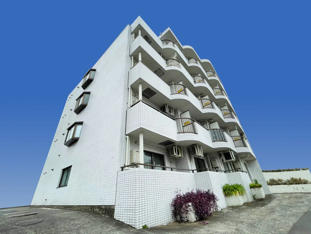 青い空を背景に建つ、白いタイル張りの外壁が特徴的なマンションの外観